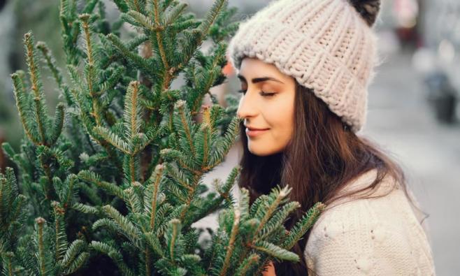 Frau mit heller gestrickter Mütze sieht sich Weihnachtsbäume an